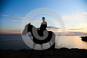 Silhouette of a girl on a horse against the background of the gentle sunset sky