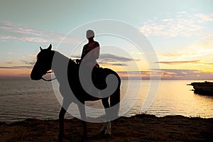 Silhouette of a girl on a horse against the background of the gentle sunset sky.