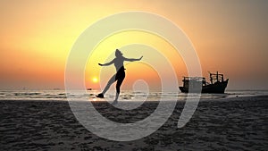 Silhouette of a girl joyfully jumping at sunset on the ocean near to the ship