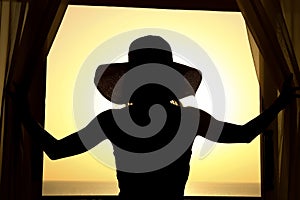 Silhouette of a girl on a loggia balcony background. A happy woman with a hat in her hands while on vacation traveling