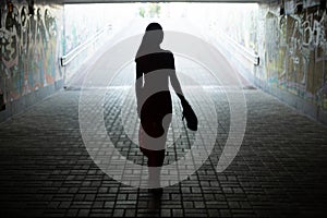 Silhouette of a girl in a long dress against the background of an exit from an underground pedestrian crossing.