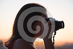 Silhouette of girl photographer taking picture setting sun on compact camera. sunset background