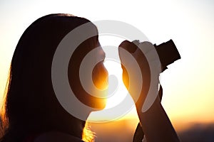 Silhouette of girl photographer taking picture setting sun on compact camera. sunset background