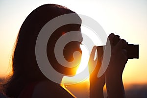 Silhouette of girl photographer taking picture setting sun on compact camera. sunset background