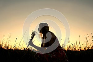 Silhouette of Girl Picking Flowers in Meadow at Sunset