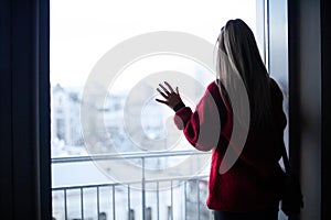 Silhouette of a girl in a red sweater near the window and city view. Depression and loneliness. Toned