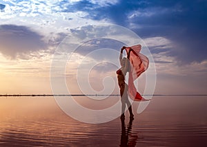 Silhouette of a girl in a red swimsuit on the beach. Red tissue develops in her hands