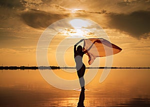 Silhouette of a girl in a red swimsuit on the beach. Red tissue develops in her hands