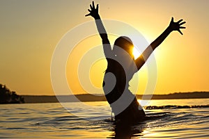 Silhouette of girl in a rive at sunset with hands up in the air. Summer vacation