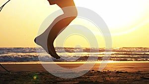 Silhouette of girl`s legs jumping on the rope on the sea sand beach at sunset.