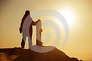 Silhouette of girl snowboarder stands against sunset sky