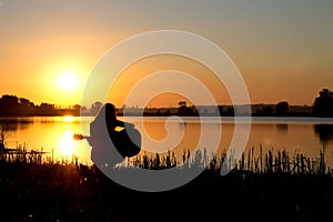 Silhouette of a girl at sunrise playing the guitar by the river