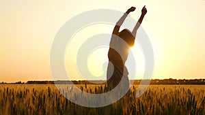 Silhouette of a girl at sunset. A young woman stands in the middle of a wheat field and raised her hands up, spinning in