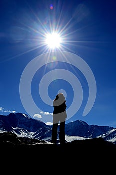 Silhouette of a girl on the top of the mountain against a sun and blue sky. Hiking. Caucasian ridge