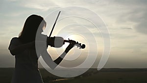 Silhouette girl violinist playing the violin at sunset sky background.