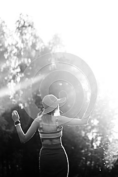 Silhouette of girl walking in park outdoor. Sunny summer lifestyle concept. Woman in dress and hat in field with