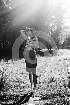 Silhouette of girl walking in park outdoor. Sunny summer lifestyle concept. Woman in dress and hat in field with