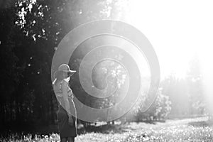 Silhouette of girl walking in park outdoor. Sunny summer lifestyle concept. Woman in dress and hat in field with dandelions. Light