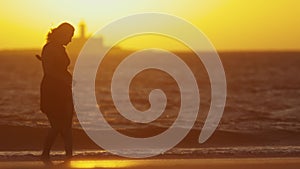 Silhouette of graceful young woman dancing on the seashore during bright orange sunset