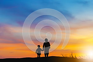 Silhouette of grandmother and grandchild looking sun down and walking on the beach evening sunset background, Happy family concept