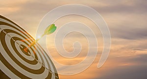 Silhouette of green dart arrow hitting bullseye target center dartboard on sunset background. Business targeting and focus concept