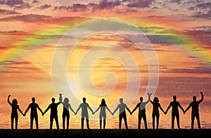 Silhouette of a group of happy people holding hands by the sea at sunset with a rainbow