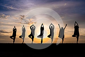 Silhouette of group of people doing yoga during colorful sunset or sunrise at a beach