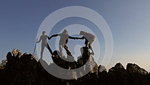 Silhouette of Group team tourists lends helping hand climb cliffs mountains helping hand. teamwork people climbers climb top