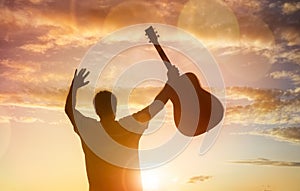 Silhouette of guitarist musician holding guitar against sunset