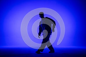 Silhouette of guy in casual clothes dancing elements of hip hop in studio with blue light. Dancer demonstrates body