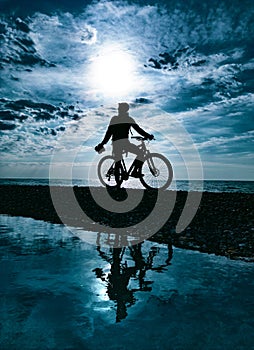 silhouette of a guy on a mountain bike against the background of the sea and beautiful textures of clouds