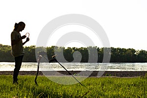 Silhouette of a guy who puts on wireless headphones.  In front of him stands a wireless metal detector supported by a shovel.