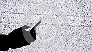 Silhouette of a hand holding a smartphone on tv screen background with white static noise