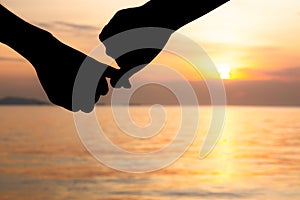 Silhouette of hand to pinky promise, pinky swear in front of the sun during sunset time. Love and valentine concept