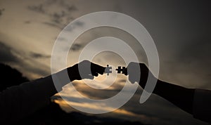 Silhouette of hands holding jigsaw puzzles and joining together at sunset background