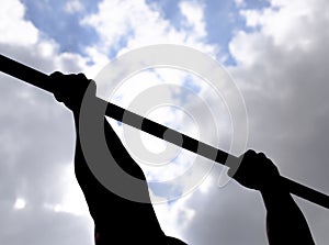 Silhouette of hands on a horizontal bar. Hands on the bar close-up. The man pulls himself up on the bar. Playing sports in the fre