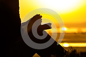 Silhouette of the hands of woman praying to God in the nature witth the Bible at sunset, the concept of religion and spirituality