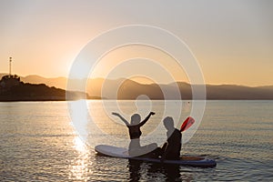 Silhouette of happiness boy and girl sitting on sup surf at the ocean. Concept lifestyle, sport, love