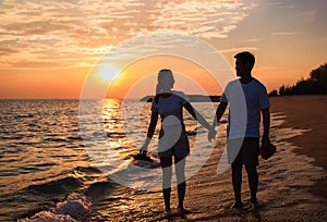 Silhouette of happy Asian couple hands holding and walk together on the beach while golden sunset time evening