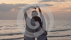 Silhouette of happy asian couple love gesture heart shape symbol of hand on the beach in vacation with romantic together.