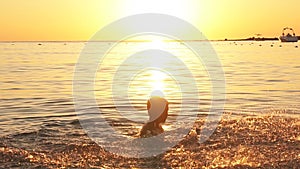 Silhouette of happy boy having fun in sea raises splashes at sunset, slow motion