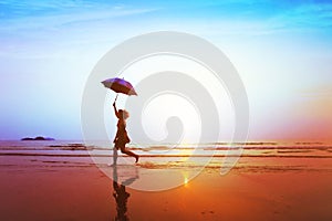 Silhouette of happy carefree girl with umbrella jumping on the beach