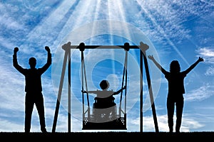Silhouette of happy child is disabled in a wheelchair on an adaptive swing with mom and dad. have fun together photo