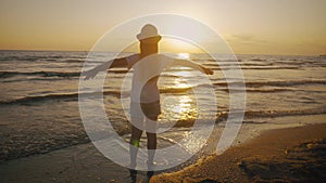 Silhouette of happy child girl stands on background of sunset sky and sea and throws his hands as if flies. Summer