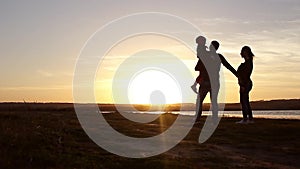 Silhouette, happy child with mother and father, family at sunset, summertime. Run, raising baby up in the air, hugs, love, playing