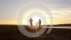 Silhouette, happy child with mother and father, family at sunset, summertime. Run, raising baby up in the air, hugs, love, playing