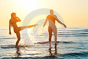 Silhouette of happy couple swimming and playing in water at sunset on beach - Young people having fun on summer time - Vacation