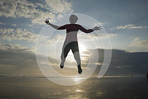 Silhouette of happy and excited woman jumping on the air above sea water at beautiful beach on sunset in freedom and excitement