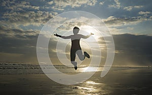 Silhouette of happy and excited woman jumping on the air above sea water at beautiful beach on sunset in freedom and excitement
