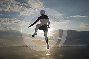 Silhouette of happy and excited woman jumping on the air above sea water at beautiful beach on sunset in freedom and excitement